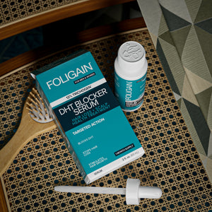 Pandangan dari atas kotak, botol dan penitis serum DHT FOLIGAIN di sebelah berus rambut.