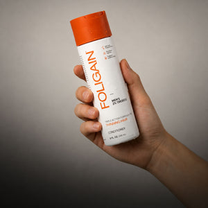 Tangan memegang perapi tiga tindakan FOLIGAIN untuk lelaki dengan 2% TRIOXIDIL.