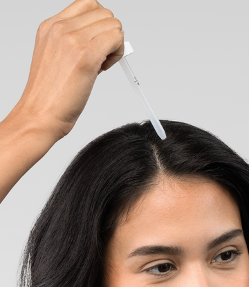 Wanita menyapu rawatan rambut cecair sepanjang belahan rambutnya dengan penitis.
