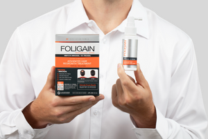 Lelaki memegang kotak dan botol semburan rawatan sapuan FOLIGAIN dengan 5% minoksidil dan 5% TRIOXIDIL.