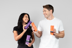 Wanita dan lelaki memegang botol penjagaan rambut FOLIGAIN berwarna ungu dan jingga.