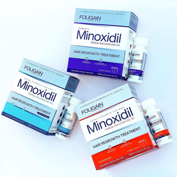 Kotak dan botol minoksidil FOLIGAIN dalam pembungkusan jingga, biru dan ungu.