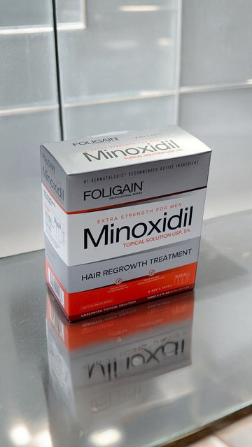 Kotak larutan sapuan minoksidil 5% FOLIGAIN di atas permukaan berpantul.