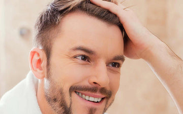 Lelaki tersenyum sambil menyisir rambut pendeknya dengan tangan.