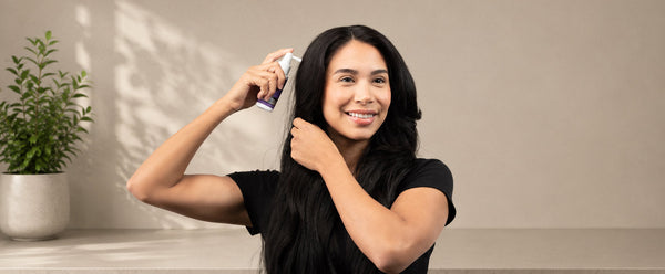 Wanita membelah rambutnya dan memegang aplikator semburan FOLIGAIN TRIOXIDIL berhampiran kulit kepalanya.